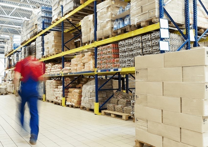 Man in red and blue overalls walking through a bright warehouse
