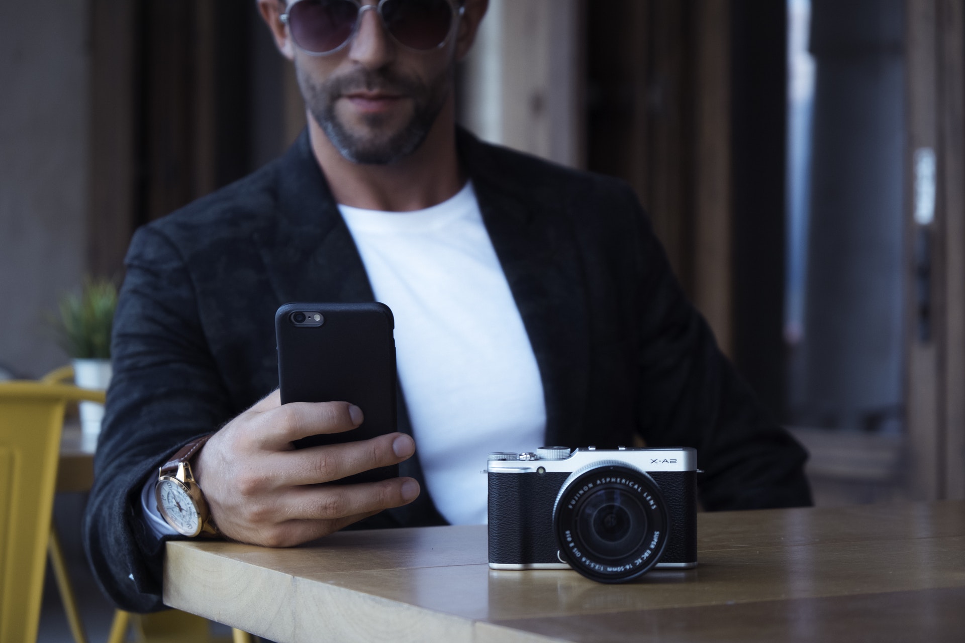 man wearing sunglasses, using smart phone, with camera atop table