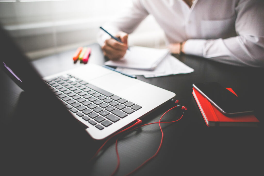 Man writing on notepad, in-front of Apple Macbook