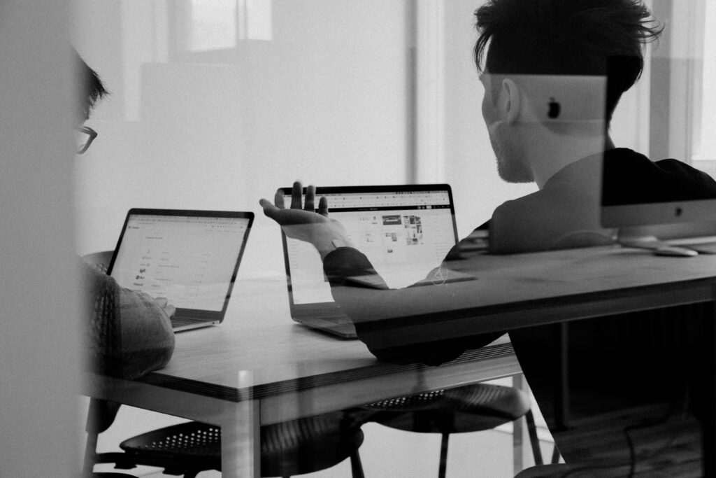 Two men working on laptops, viewed through glass