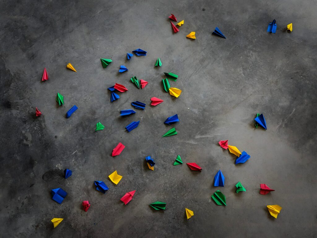 Paper aeroplanes in green, blue yellow and red, scattered across a dark stone floor
